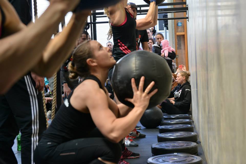 Young womens sitting at the bottom of a squat while holding up a medicine ball