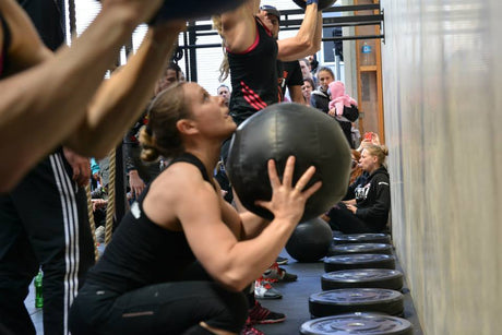 Young womens sitting at the bottom of a squat while holding up a medicine ball