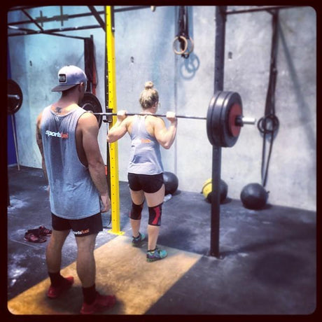 A guy spotting a girl performing a heavy back squat