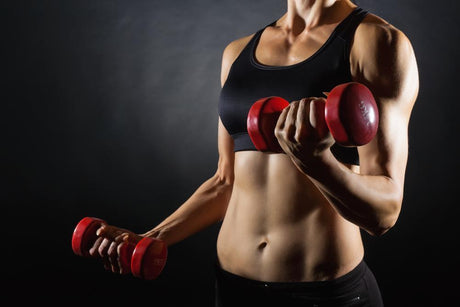 Upper woman body in black sports bra performing biceps curls with small red dumbbells