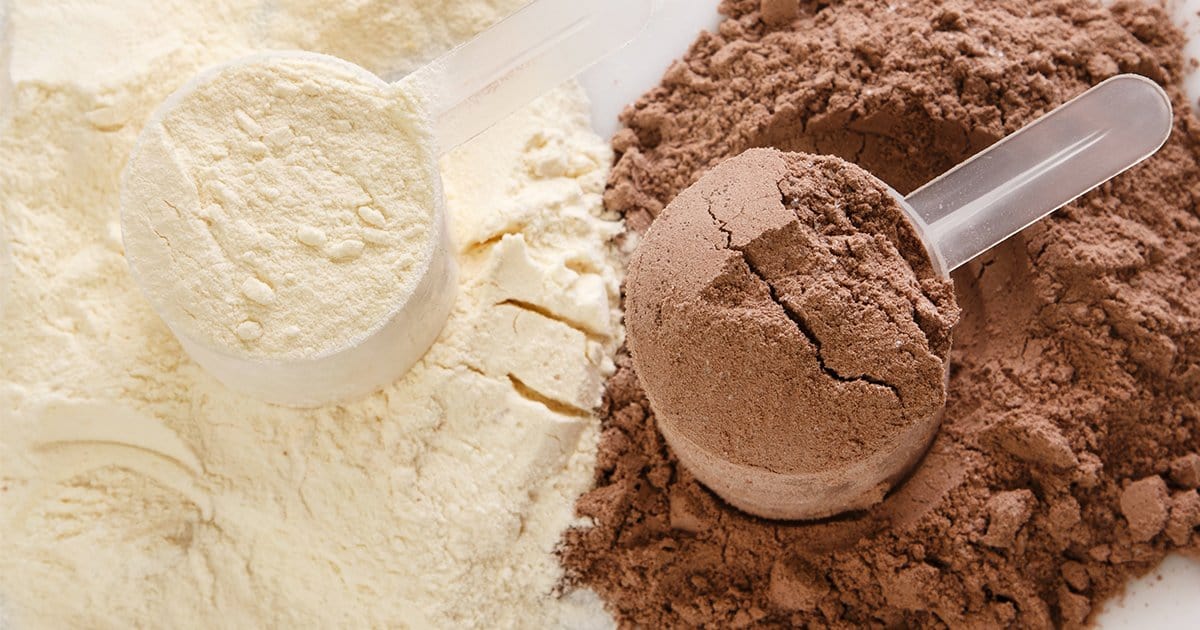 Two plastic scoops in protein powder. One filled with white powder and the other one with brown powder. 