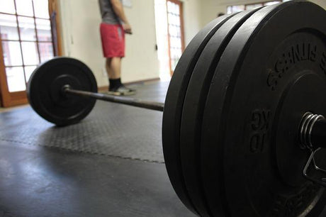 Loaded barbell in the front and a man in red shorts in the background