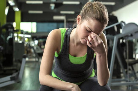 A woman sitting in the gym, pinching her brow bone in pain