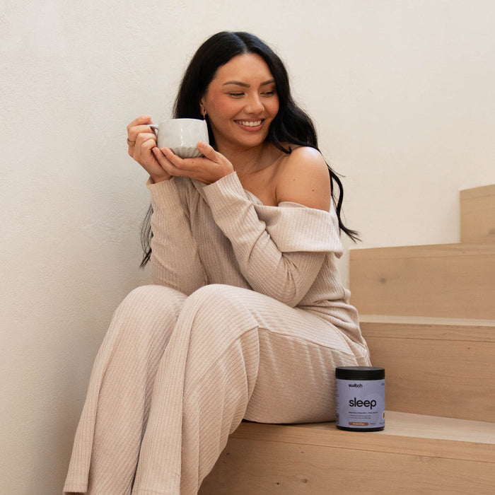 Woman sitting on wooden steps holding a mug with a product labeled 'sleep' next to her.